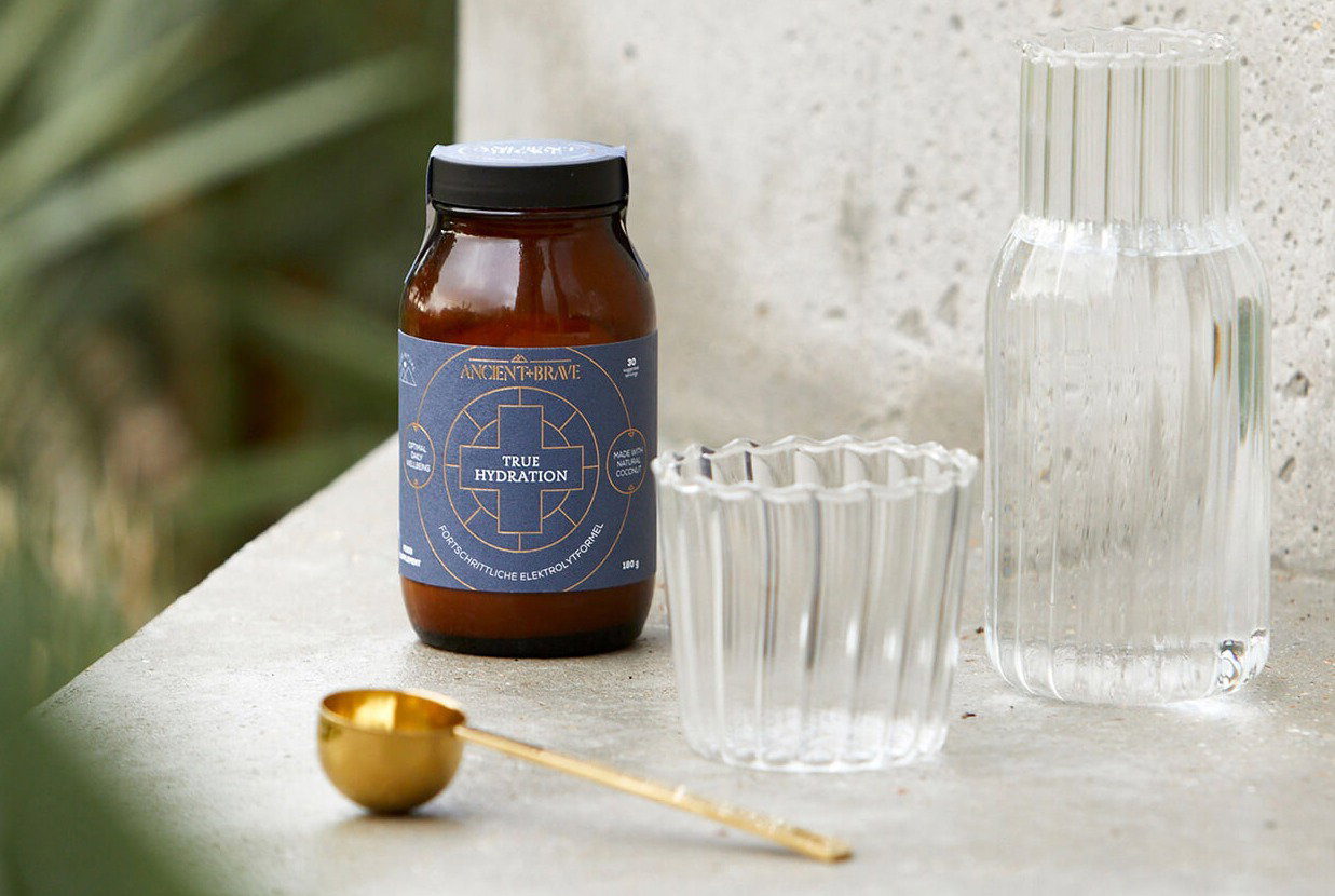 True Hydration jar, gold Ritual Scoop and a glass of water.