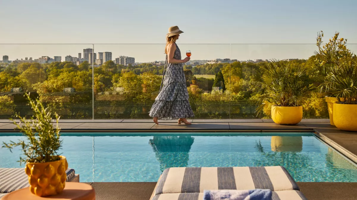 Woman walking along the side of a pool on a London hotel’s rooftop, linking to BA High Life site.