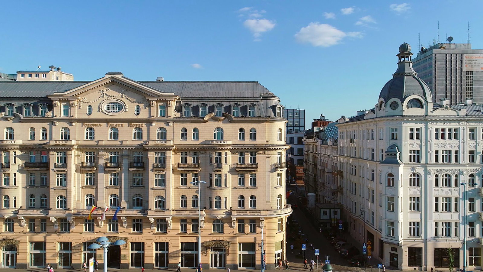 Ornate beige and white historic European buildings flanking a narrow city street under a clear blue sky