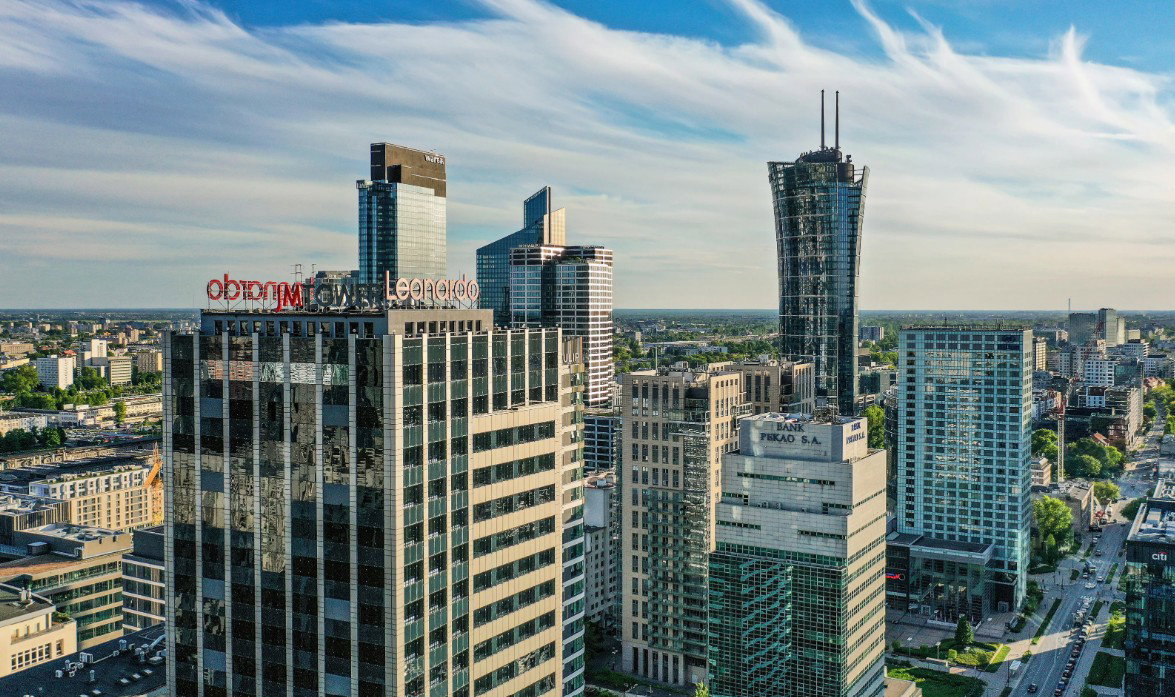 Aerial view of a modern city skyline with glass skyscrapers and high-rise office buildings beneath a blue sky with wispy clouds