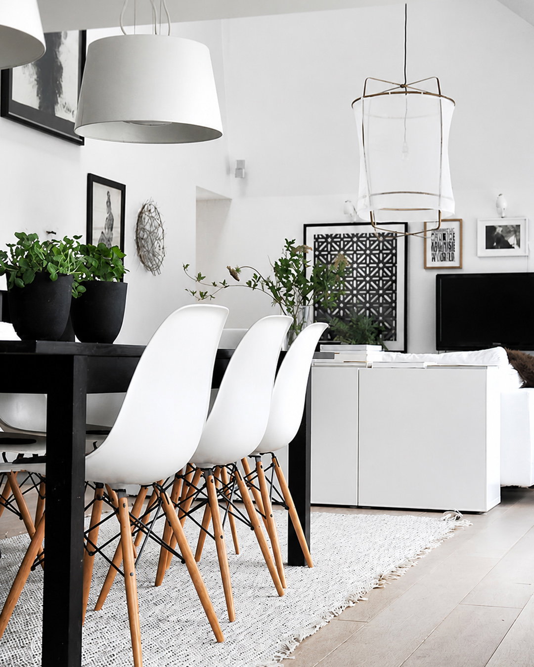 Modern Scandinavian dining area with white moulded chairs on wooden legs, black table, pendant lamps and indoor plants