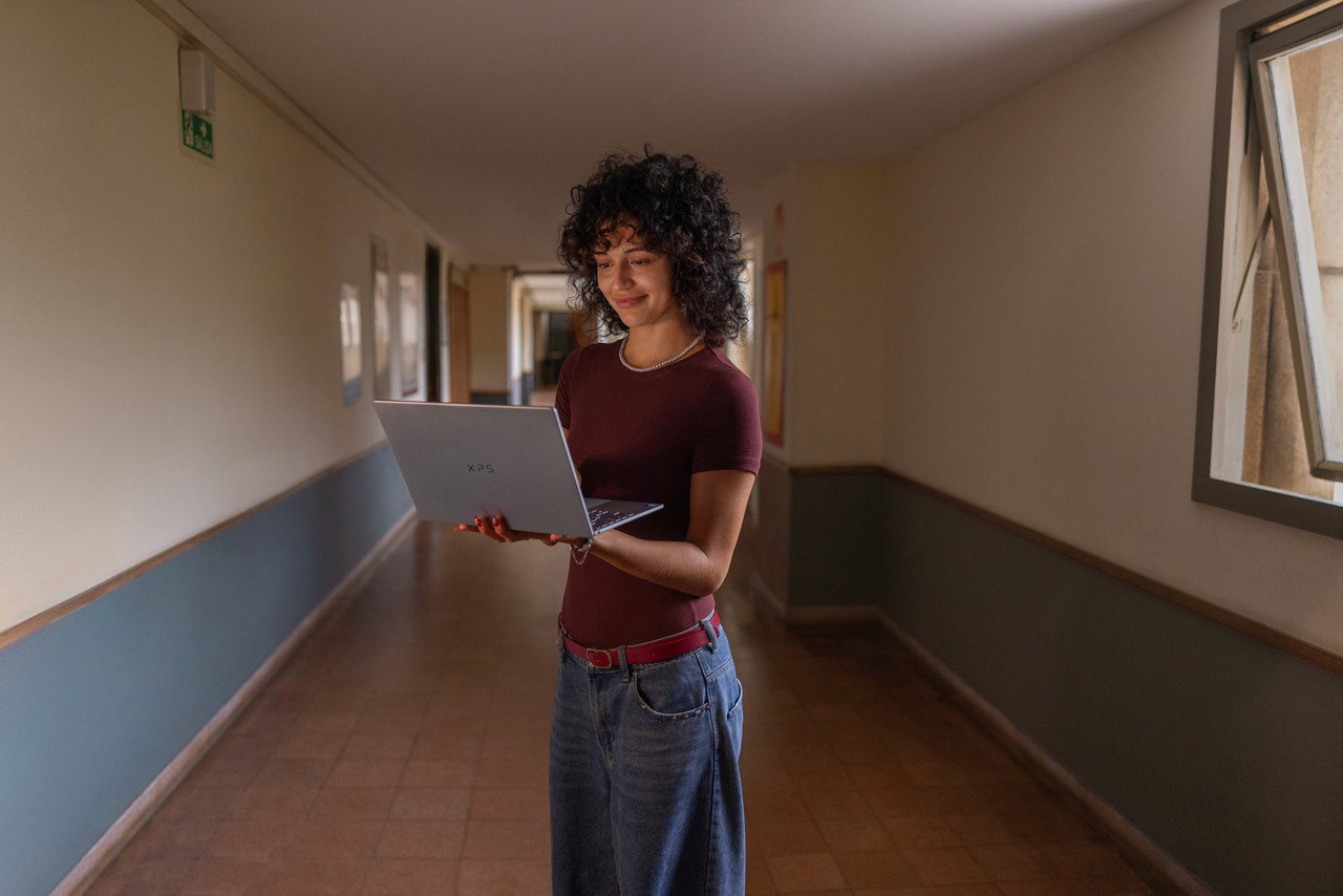 Student on the go using a Dell XPS laptop while walking through her dorm hallway.