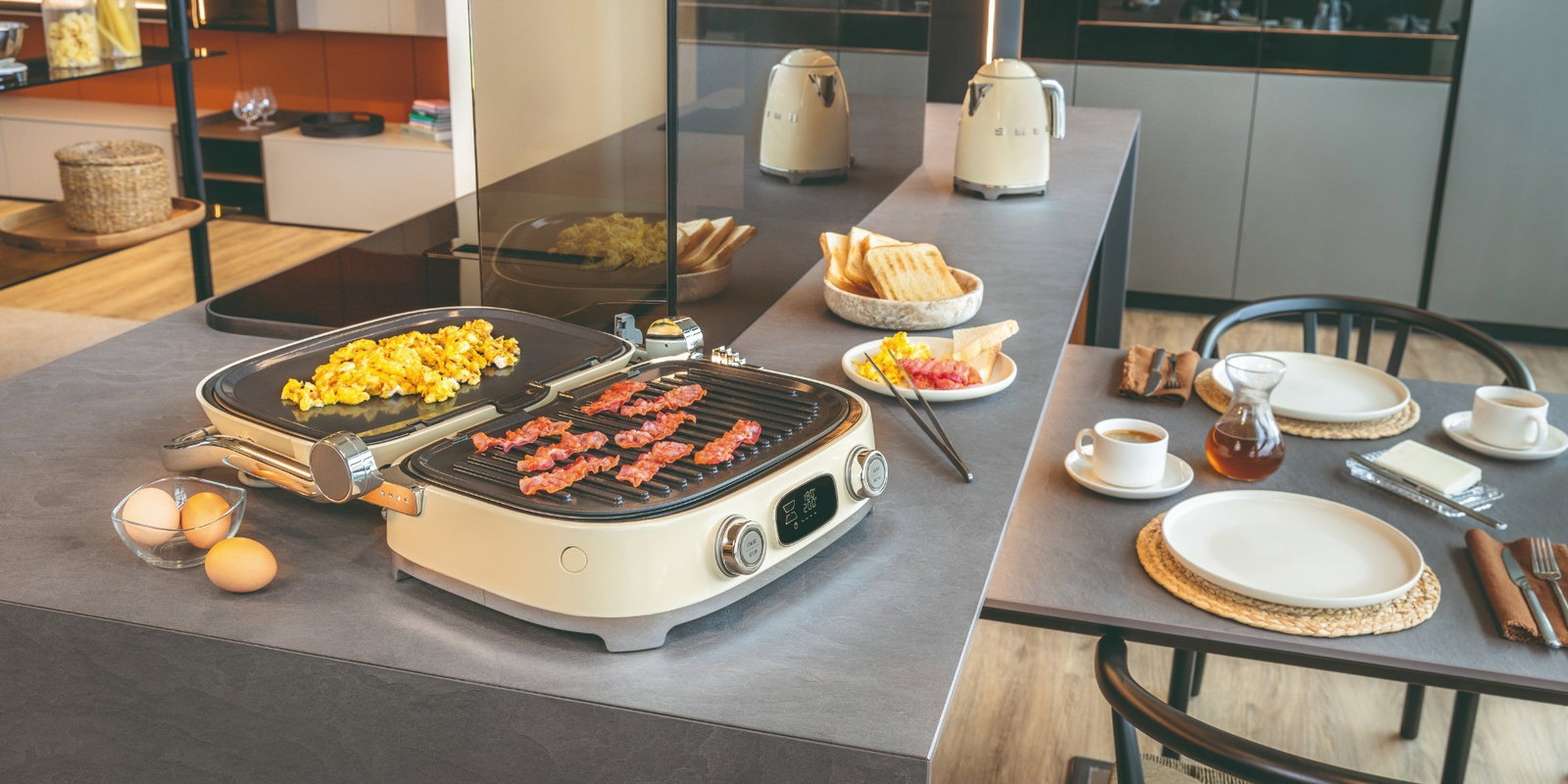 Grill Multiusos Smeg abierto en modo barbacoa, con placa grill y placa lisa para cocinar beicon y huevos revueltos sobre una isla de cocina