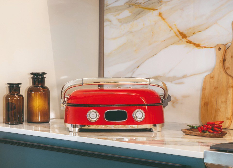 Grill Multiusos Smeg rojo cerrado sobre una encimera en una cocina contemporánea