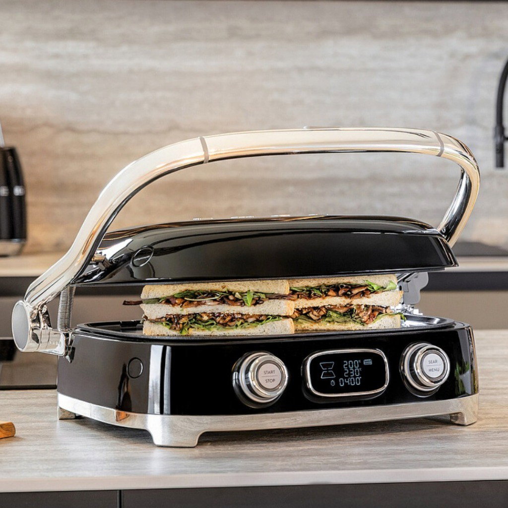 Grill Multiusos Smeg tostando sándwiches rellenos con la tapa parcialmente cerrada sobre una encimera