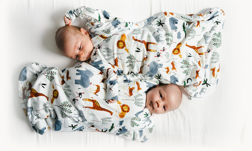 two newborn babies lying side by side wearing sleep suits with a safari animal print