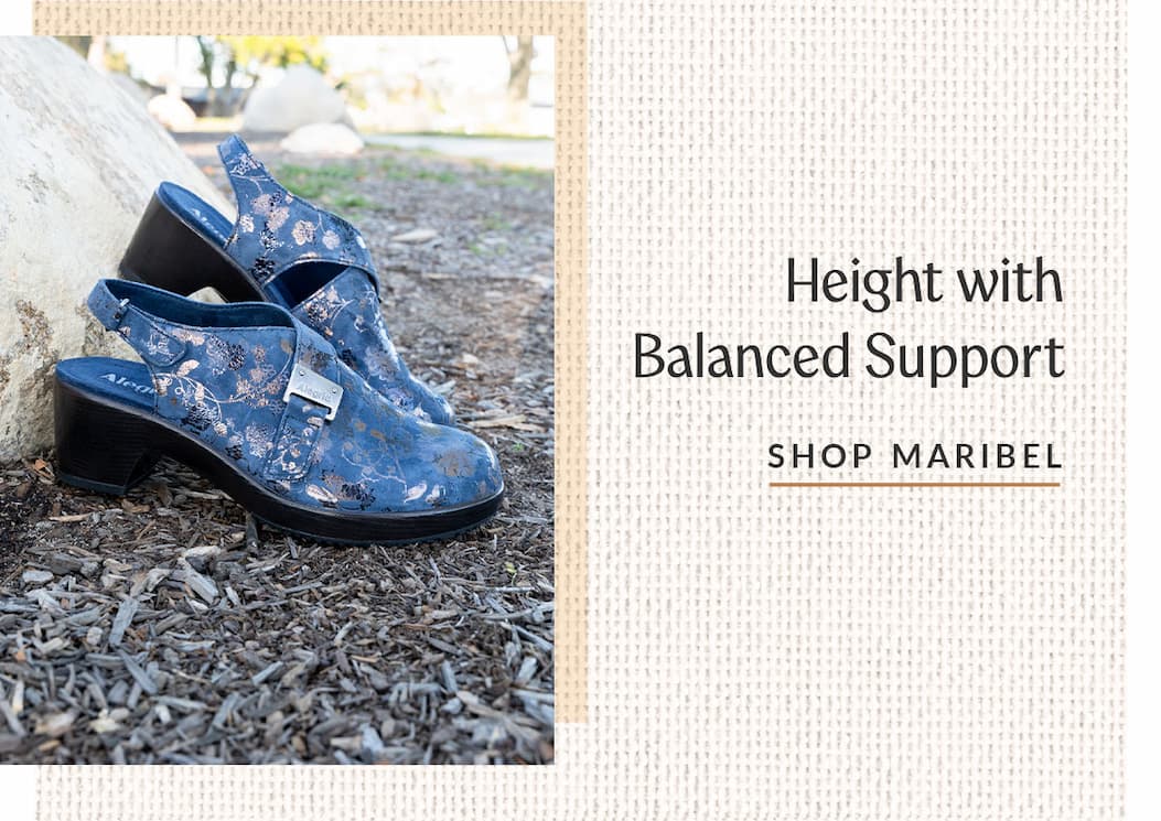 A pair of navy metallic floral Alegria Maribel heel sandals outdoors on mulch. Text reads "Height with Balanced Support."