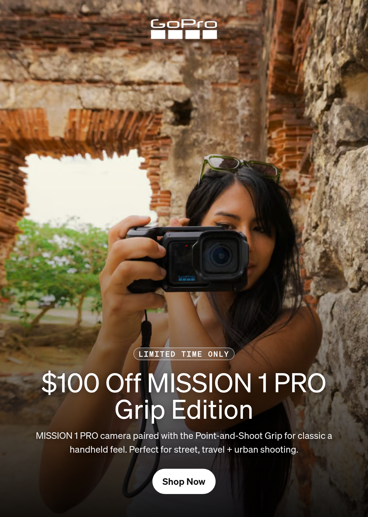 A woman holding a GoPro camera against an ancient stone wall.
