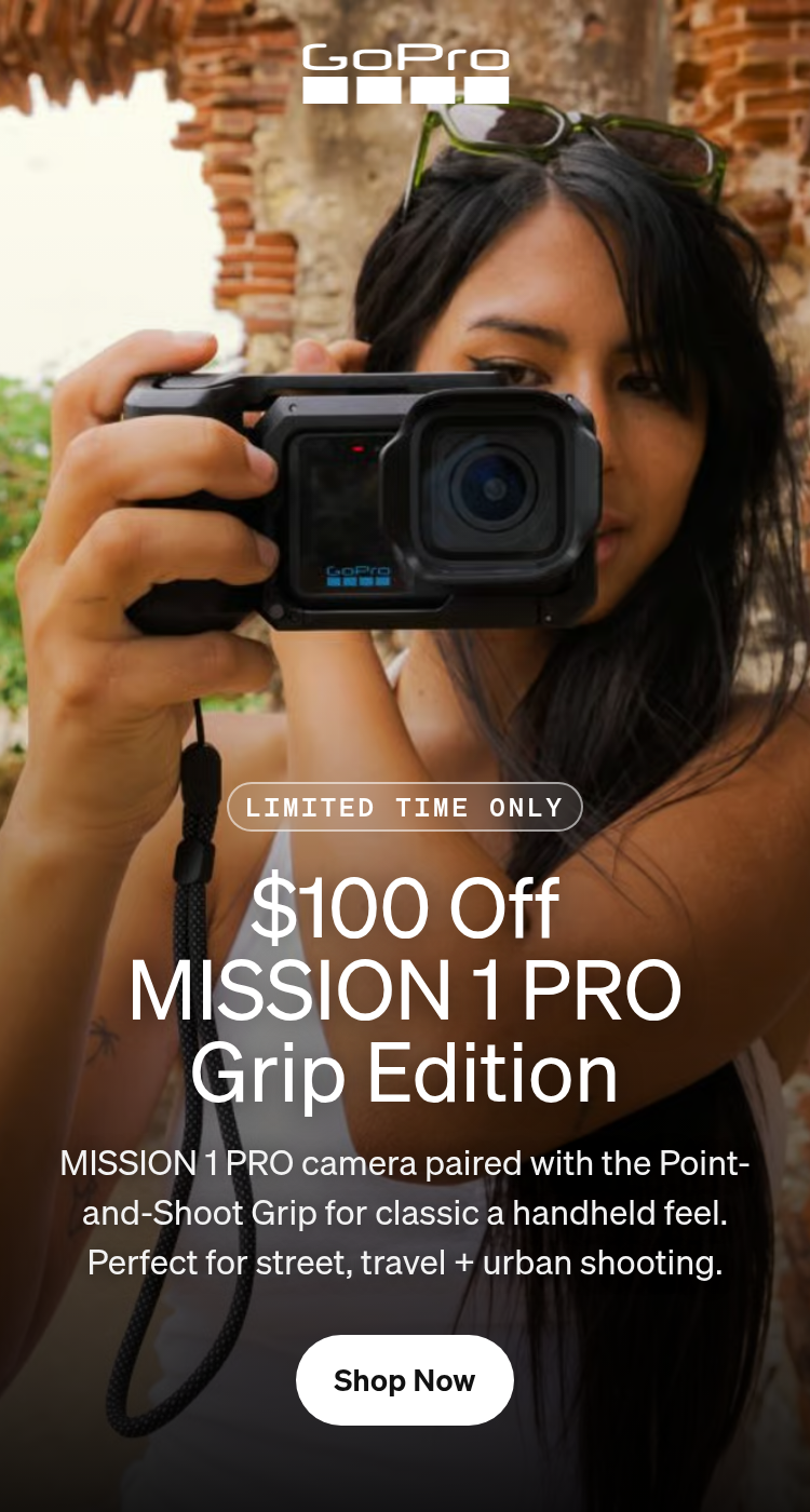 A woman holding a GoPro camera against an ancient stone wall.
