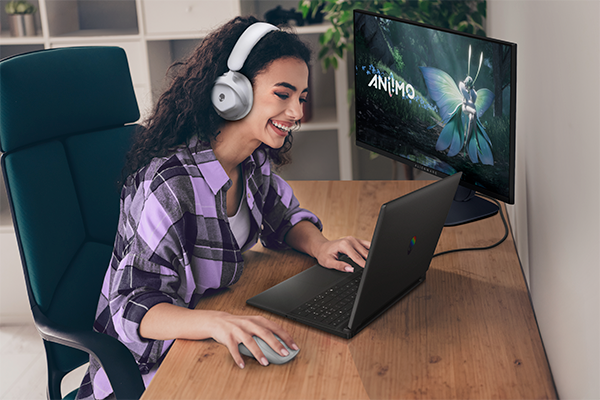 Student using Alienware laptop with monitor, keyboard, mouse, and headset at a wooden desk in a home office.