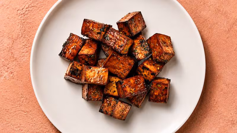Glossy caramelized cubes of marinated tofu on a white plate.