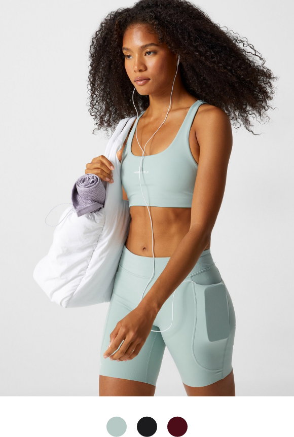 A young woman is wearing a light green racerback sport bra from INNER SELF, at $55.00
