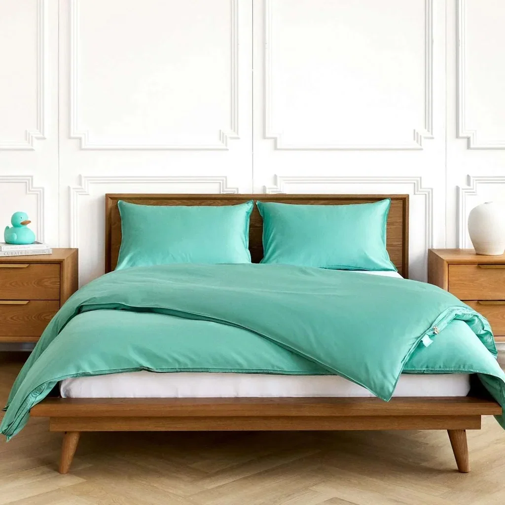 A mid-century modern wooden bed with turquoise bedding and pillows in a minimalist bedroom with white paneled walls.