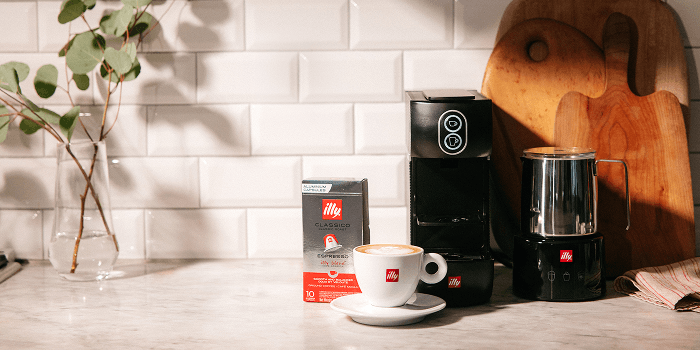Freshly brewed illy coffee served beside a coffee maker and Classico coffee on a kitchen countertop