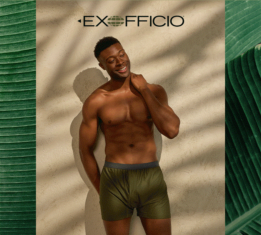 Exofficio logo at top, smiling man wearing olive green boxer shorts standing against a textured wall with leaf shadows.