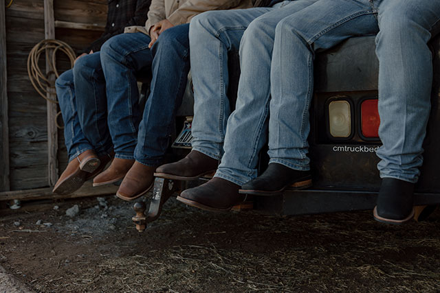 A group of men wearing Justin jeans while sitting in the back of a pick-up truck.