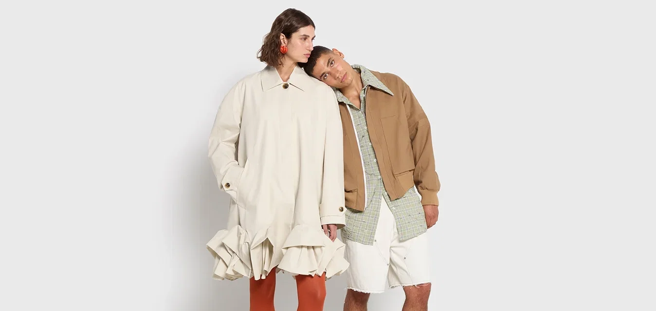 Robe crème à volants, collants orange, chaussures noires. Veste marron sur une chemise à carreaux verte, shorts blancs. Fond minimaliste.