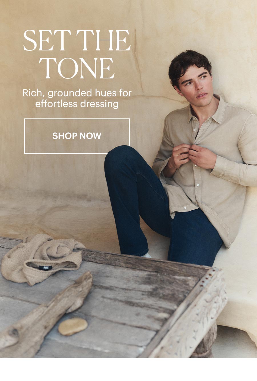 Set the Tone - Rich, grounded hues for effortless shopping. Featuring a man wearing a beige long-sleeved button-up with dark wash jeans. Shop Now.