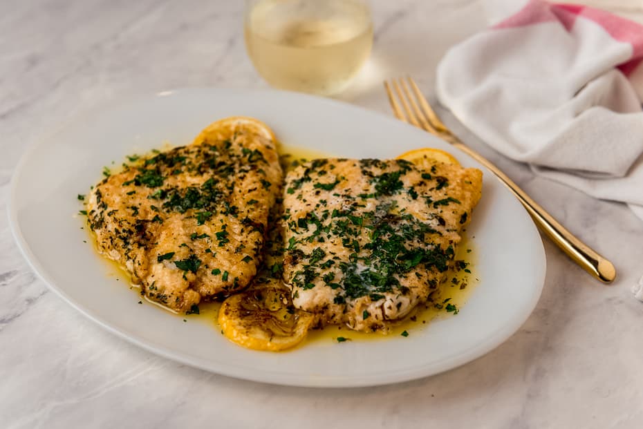 Lingcod with herbs plated with a gold fork and glass of wine