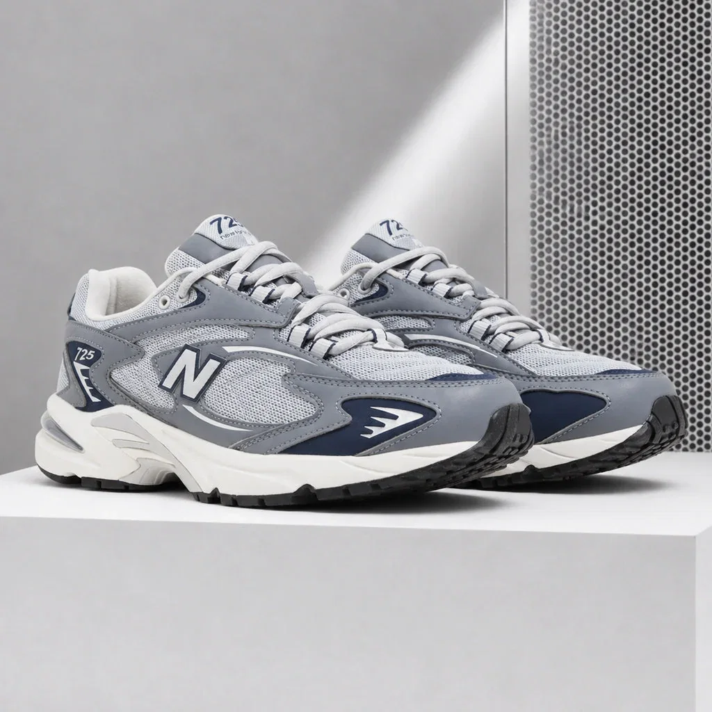 Pair of New Balance 725 sneakers in gray, navy, and white displayed on a white platform.