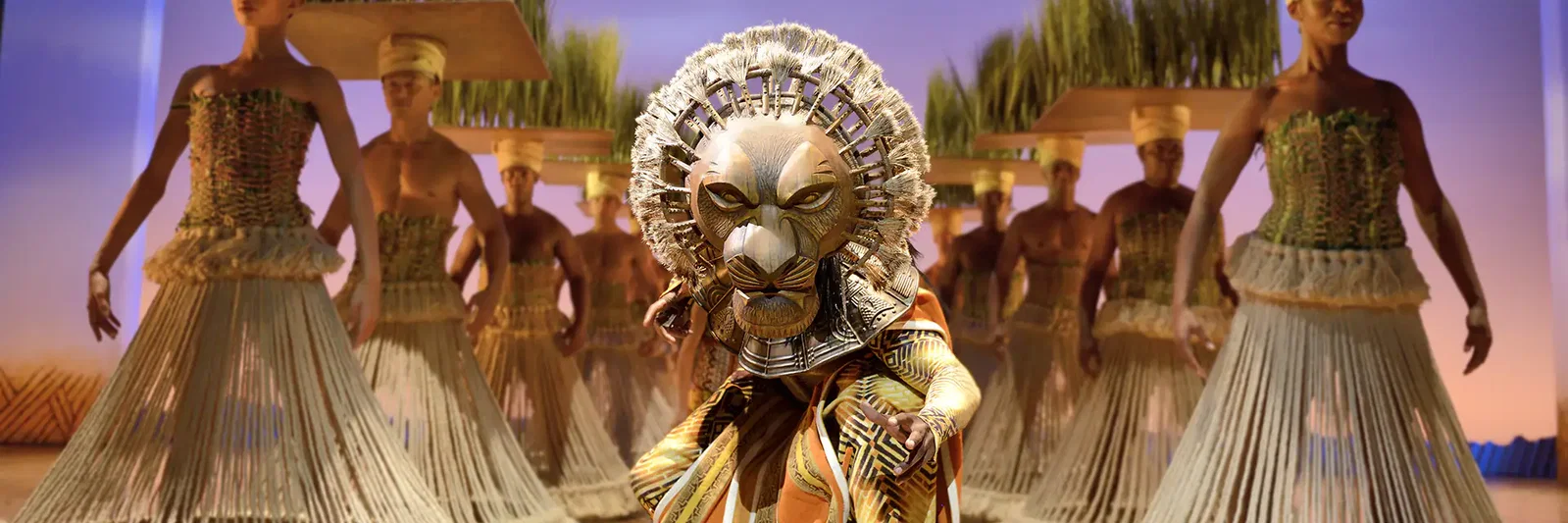 A performer in a lion costume leads a group of dancers in traditional attire on stage.