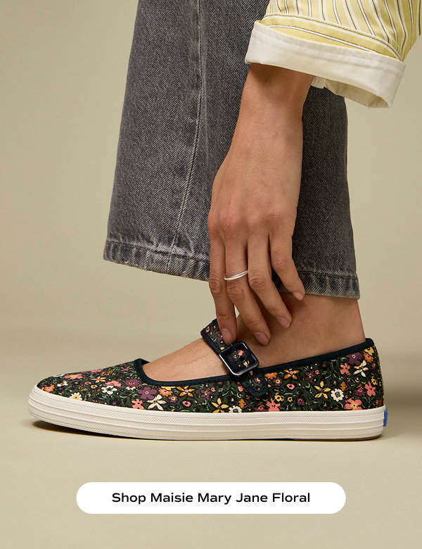 A side view of the Maisie Mary Jane Woodland Floral Canvas flats in dark teal/multi shown on foot paired with grey straight-leg jeans and a yellow cotton button up. Shop Maisie Mary Jane Floral.