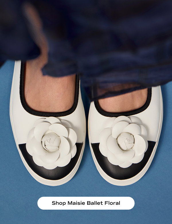 A top-down view of a pair of Maisie Ballet Toe Cap Leather Flower Applique flats in egret/black shown on foot paired with a silk navy blue maxi skirt. Shop Maisie Ballet Floral.