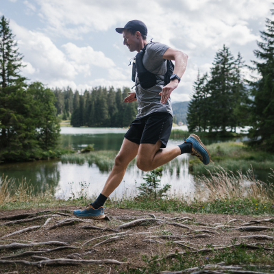 Trail runner leaping over a root on a lakeside trail