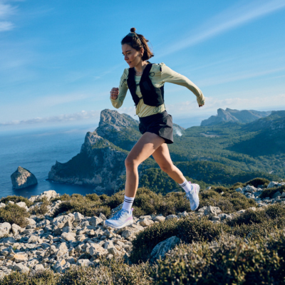 Trail runner leaping over a rock on a rocky path overlooking the ocean