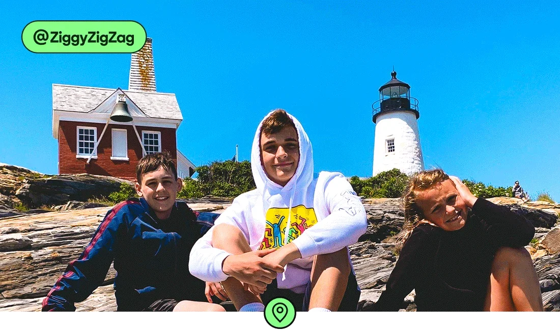 Image description: Three children sitting on rocks in front of a lighthouse in Maine, photo taken by @ZiggyZigZag
