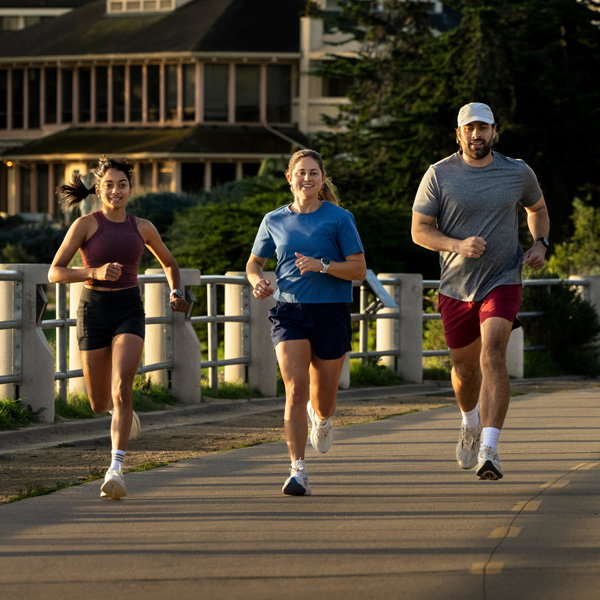 Three runners wearing performance sportswear on a paved outdoor route. Running clothing and footwear designed for comfort, support and every training goal.