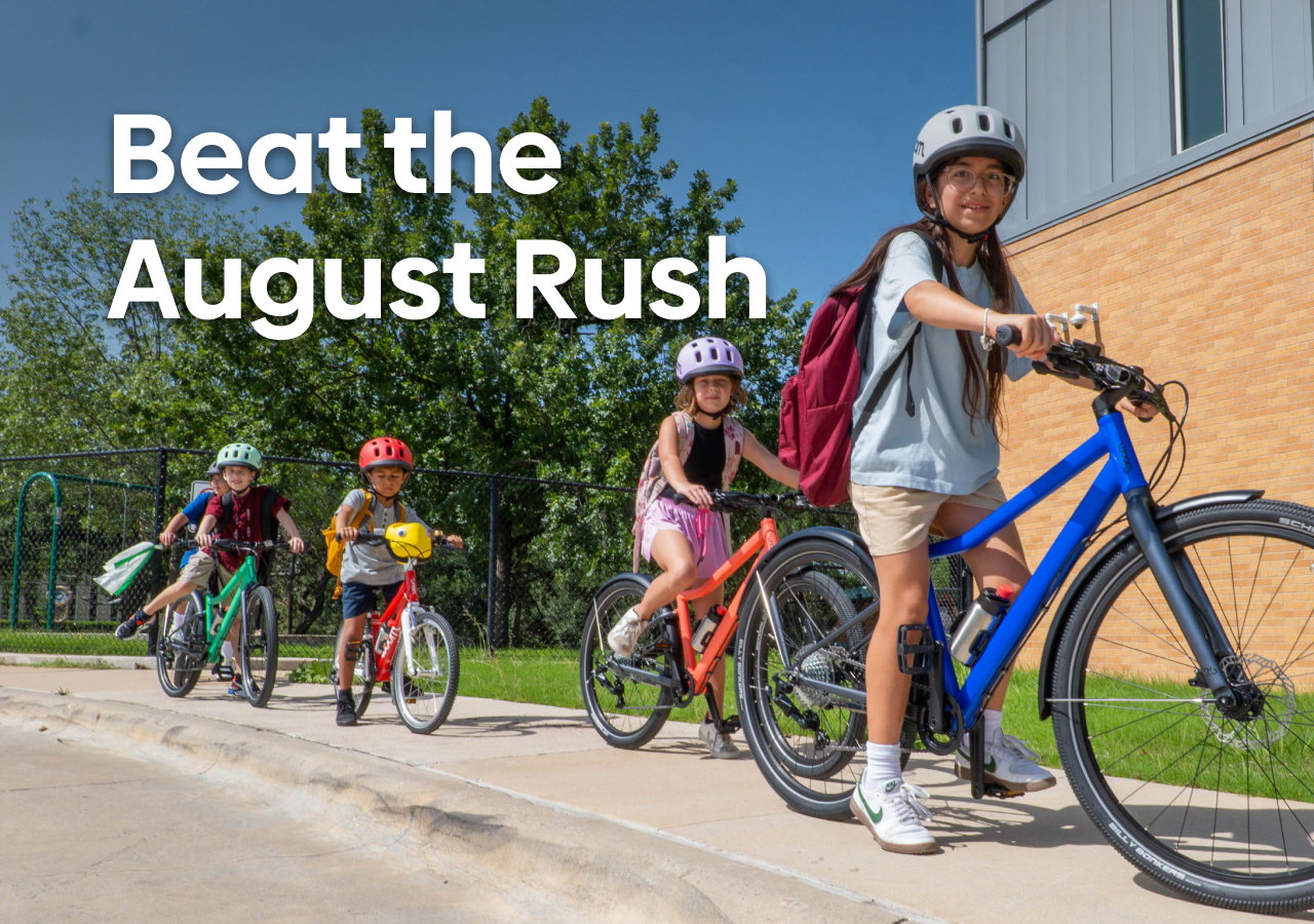 A group of kids ride their woom GO and EXPLORE bikes to school on a sunny day