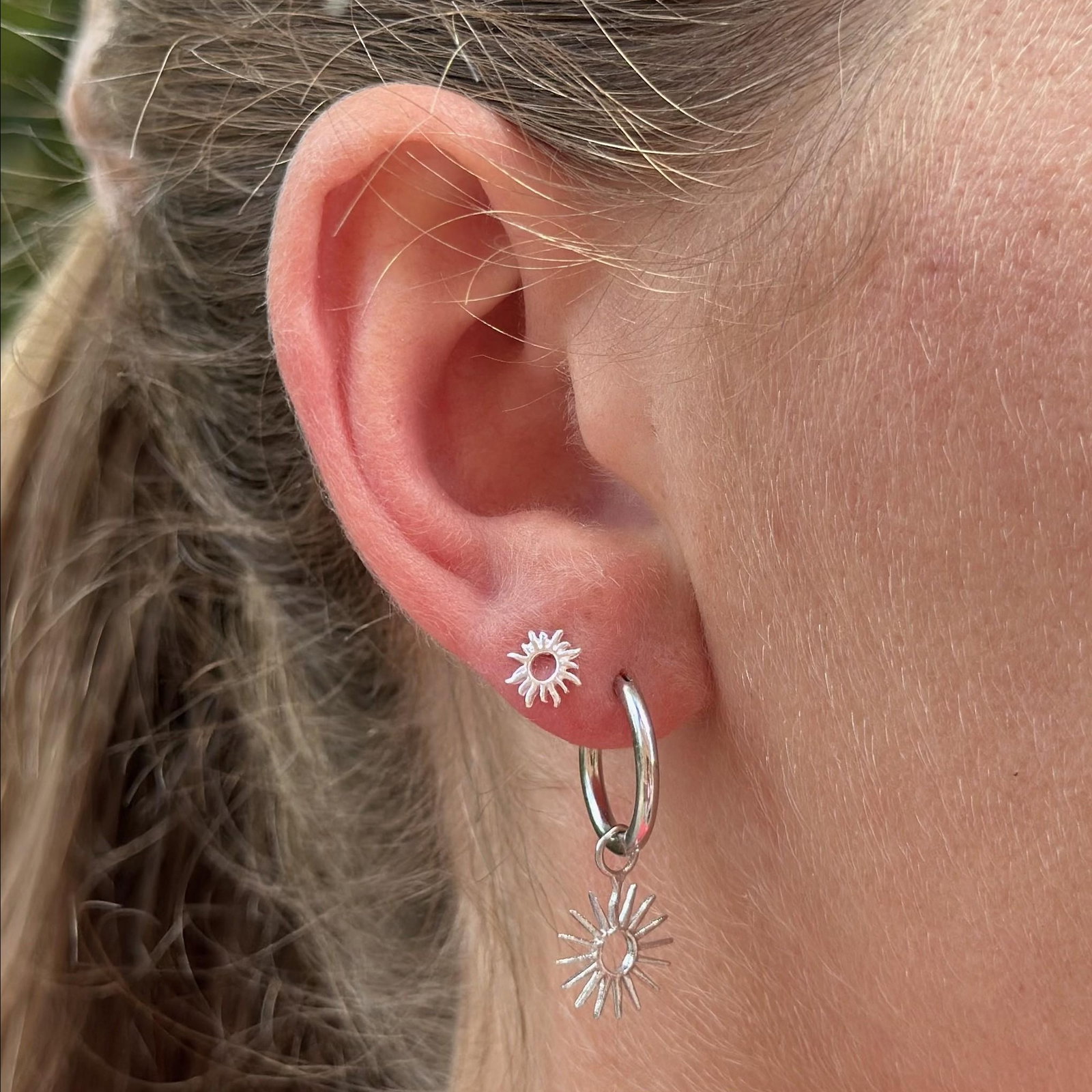 A silver sun-shaped stud earring with a post and backing.