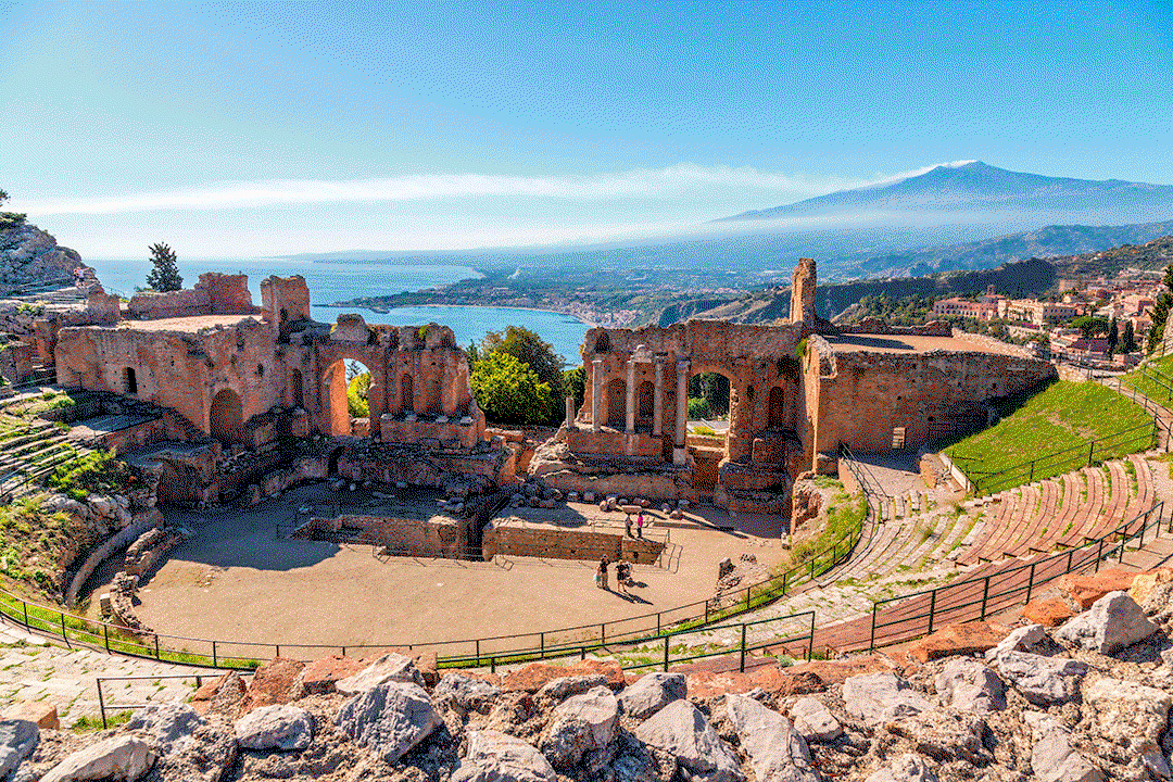 El Teatro Greco de Taormina abierto hacia la bahía de Naxos, con el Etna humeando al fondo
