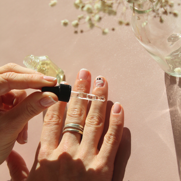 Hand applying cuticle oil with a dropper to freshly manicured nails.