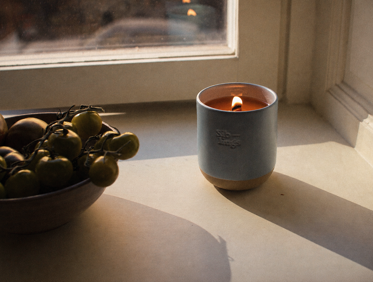 A candle burns beside a bowl of tomatoes