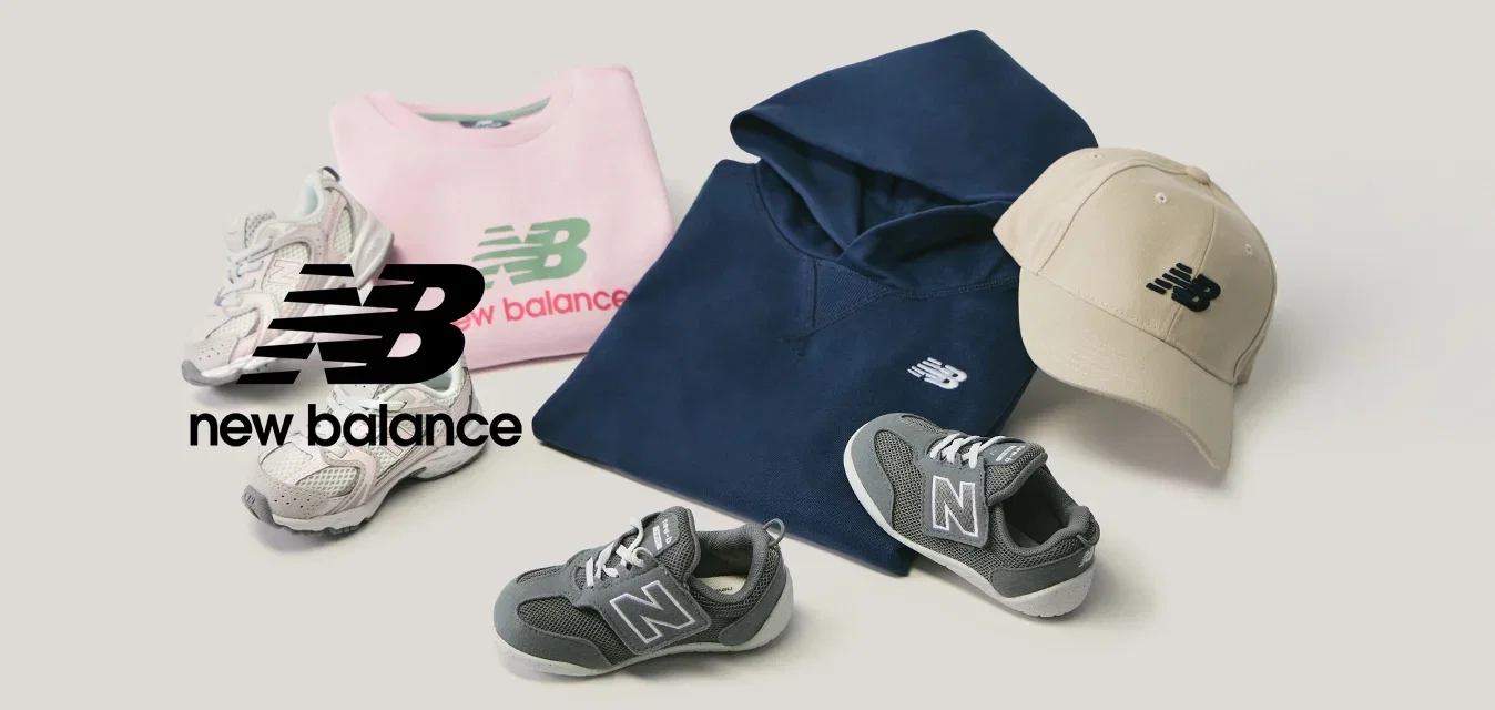 Opgevouwen roze sweatshirt, marineblauwe hoodie, beige pet, twee paar grijze sneakers op een lichte achtergrond gerangschikt.