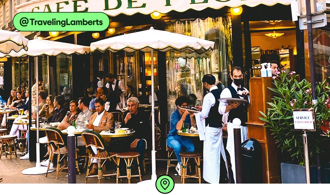 Image description: People sitting outside at small bistro tables at a Parisian cafe, photo taken by @TravelingLamberts