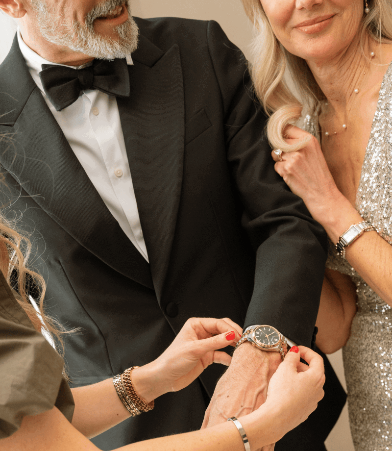 Man and woman dressed up for an event, wearing a variety of jewellery, including watches, necklaces and rings.