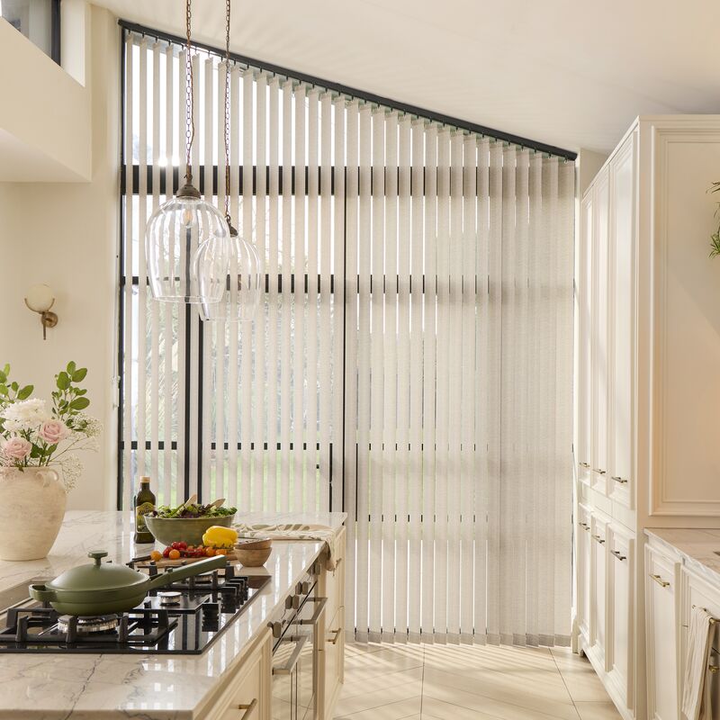 Large window dressed with pale blue Vertical blinds, filtering daylight into a modern kitchen with sage cabinets and island seating.