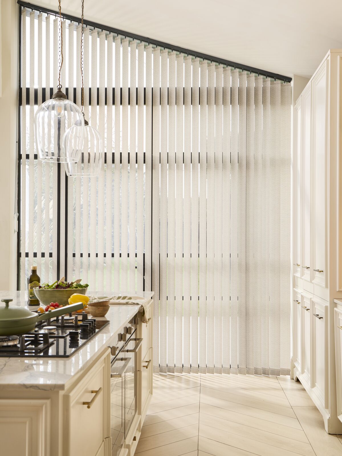 Large window dressed with pale blue Vertical blinds, filtering daylight into a modern kitchen with sage cabinets and island seating.