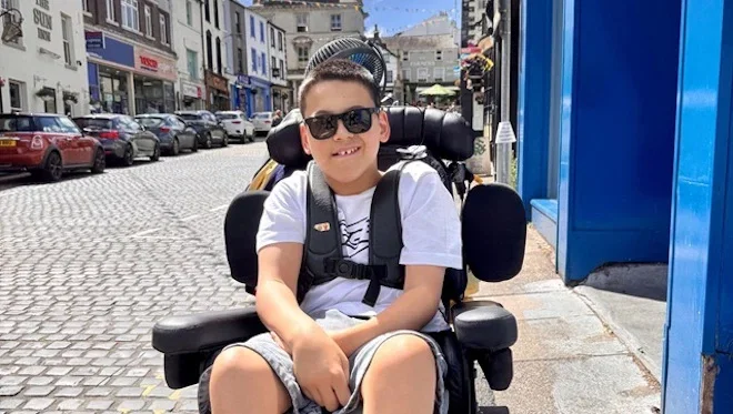 Charity fundraiser Miles, in his wheelchair with a summer street background.