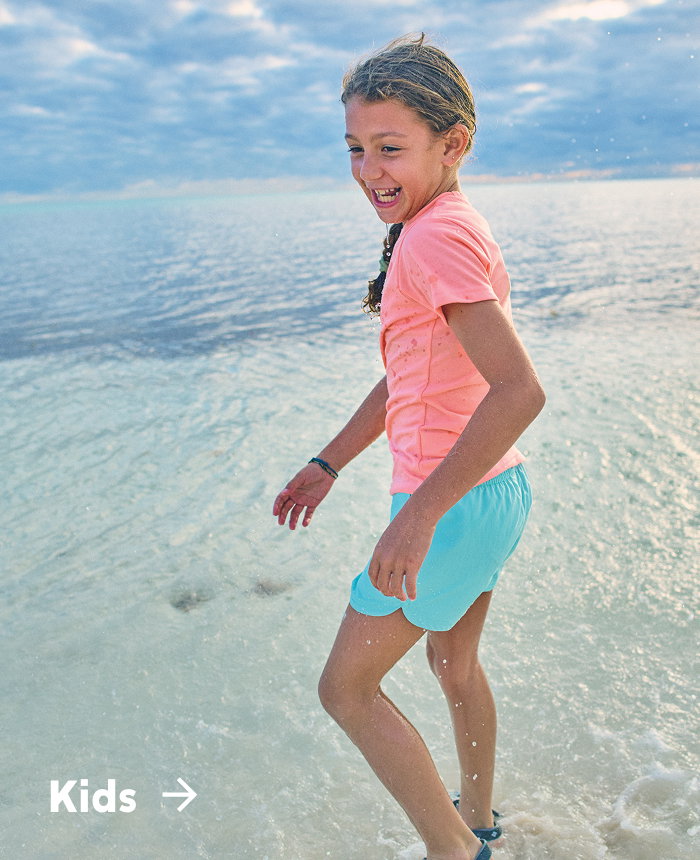 A little girl standing on the ocean shore in bright colored clothing with text: Kids