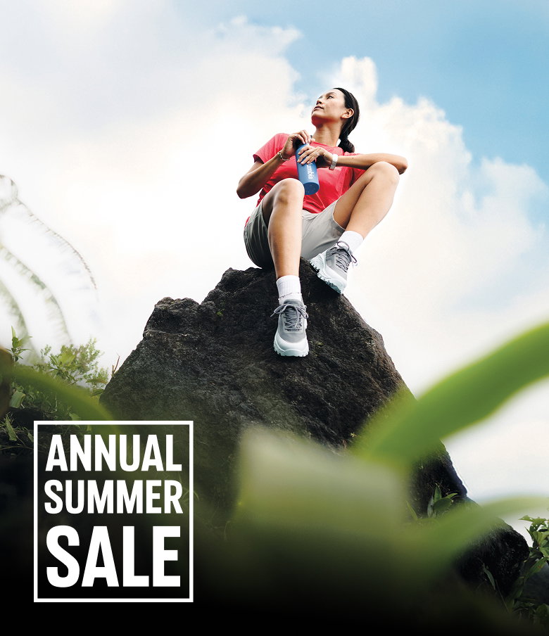 A woman sitting on a rock wearing hiking gear with text: ANNUAL SUMMER SALE