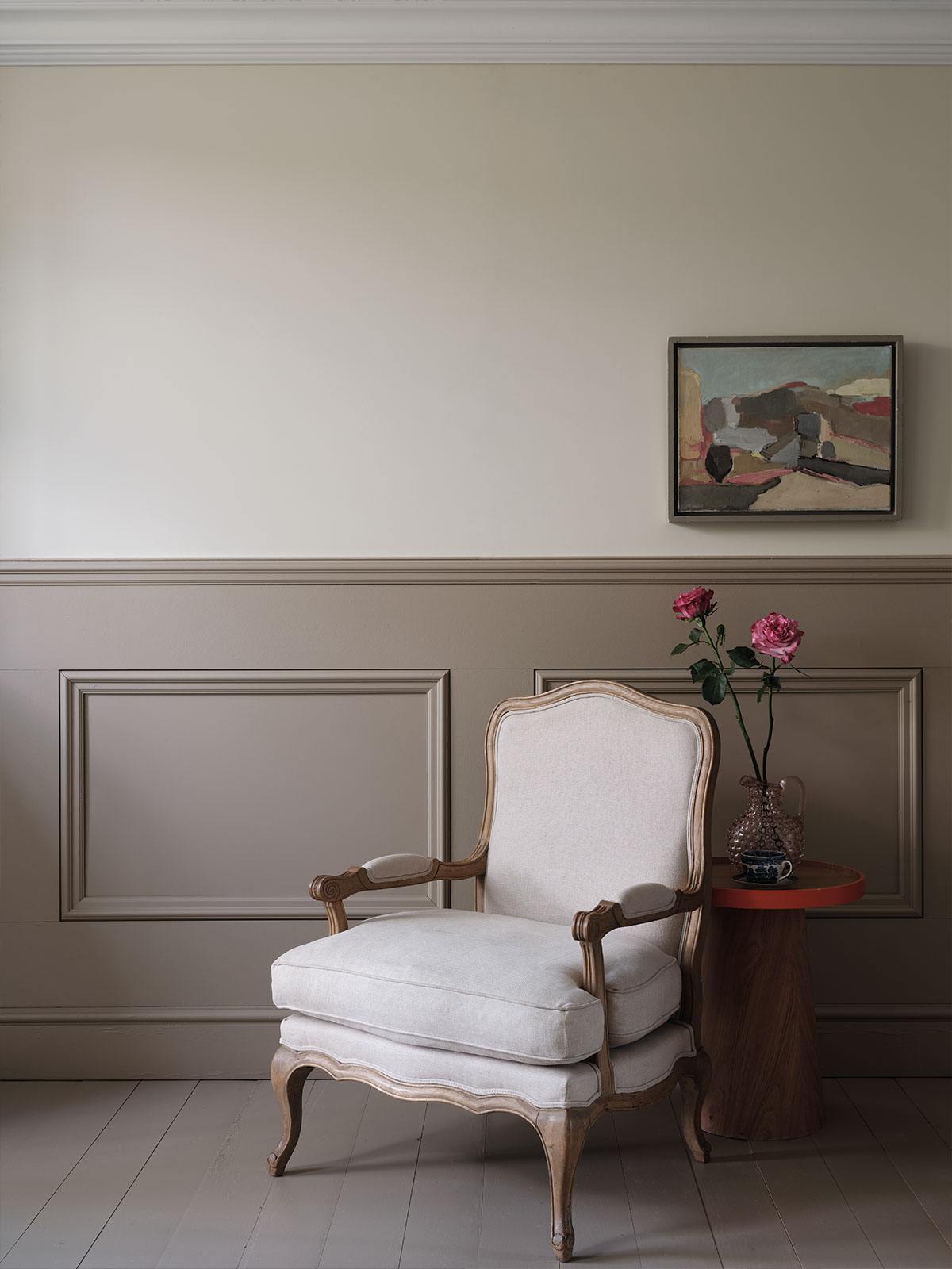 Classic sitting area with upholstered armchair, taupe panelling, and pink flowers on side table.