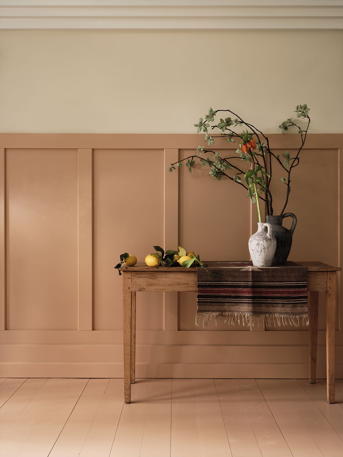 Simple beige and cream wall with wooden table, lemons, and rustic vase of branches.