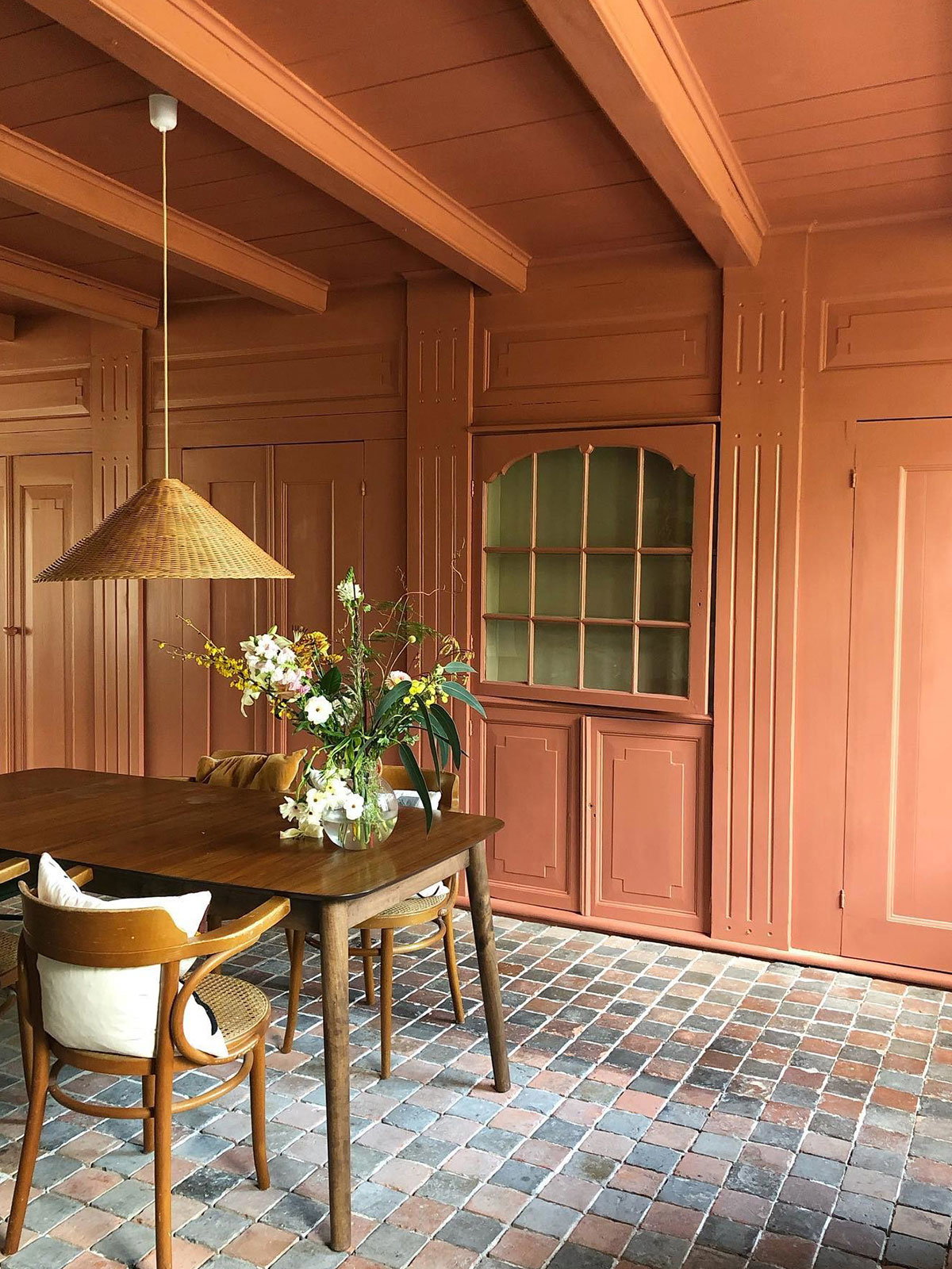 Elegant taupe dining space with wooden table, gold mirror, and sculptural chandelier.