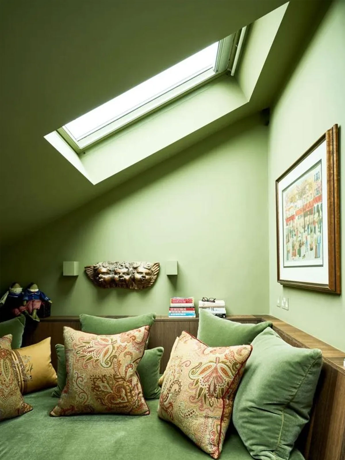 Cosy green attic nook with paisley cushions, skylight and wall art above a built‑in seat