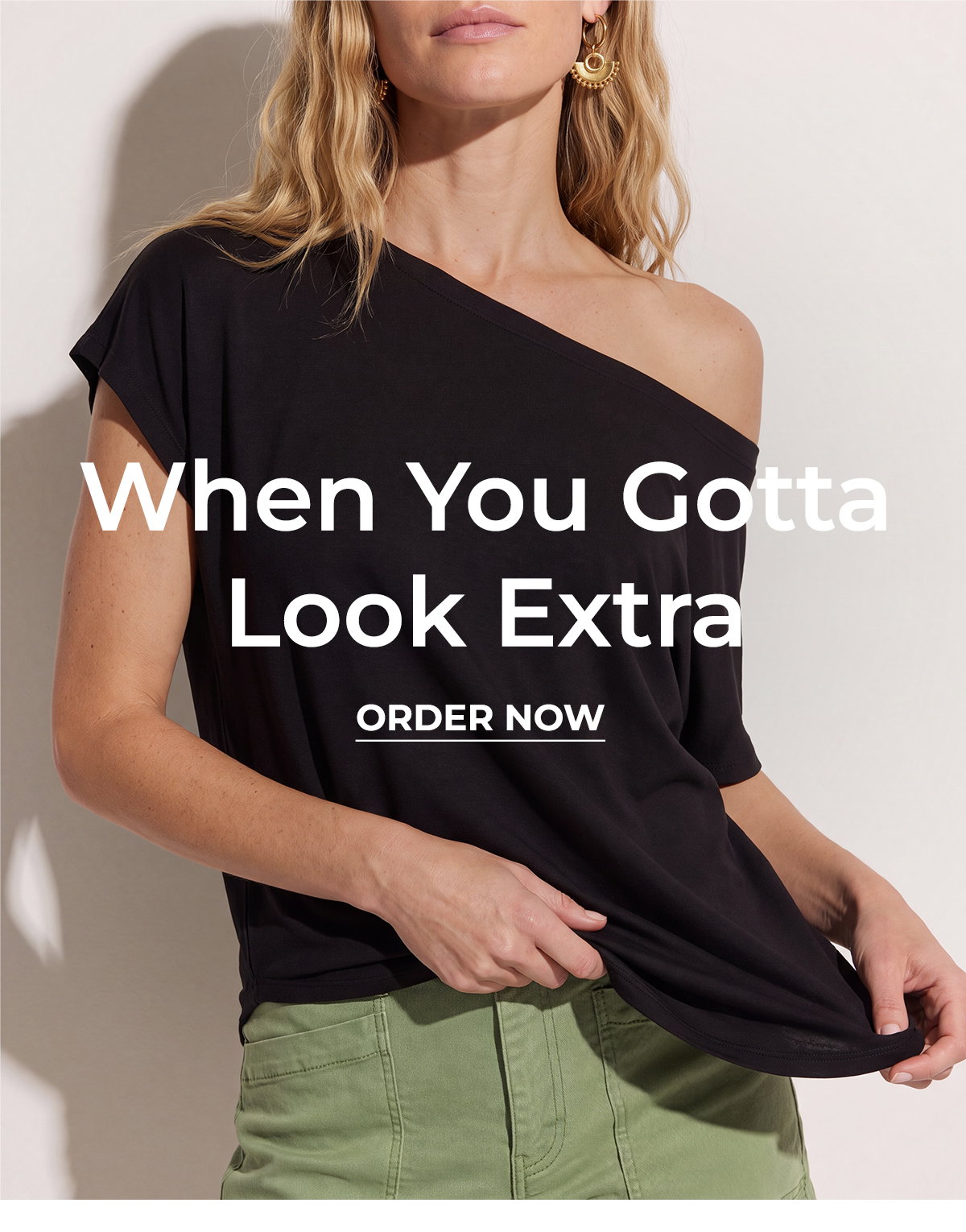 Woman models a black one shoulder top with green pants for End of Season style.