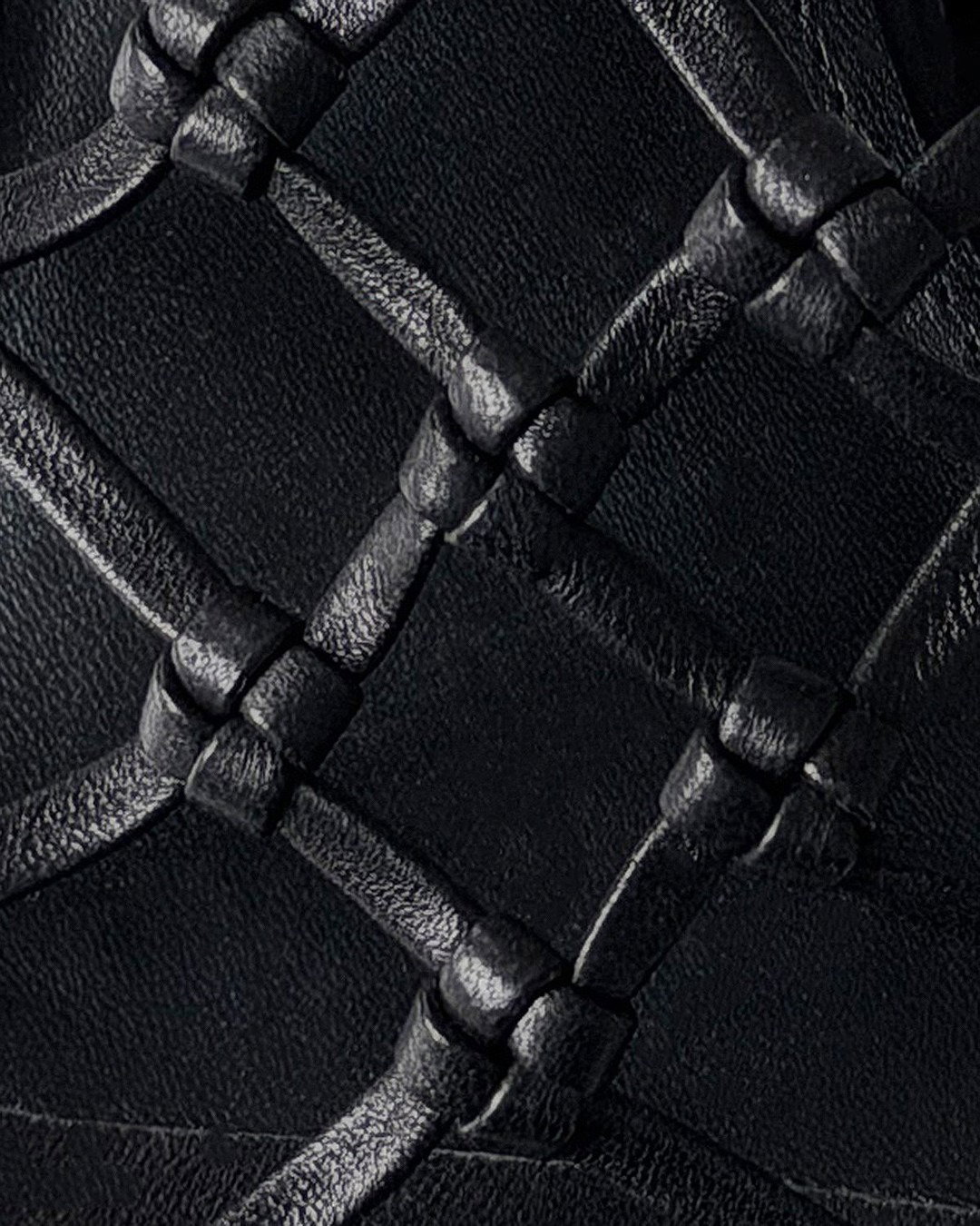 Close-up of black woven leather upholstery with knotted intersections forming a diamond quilted texture